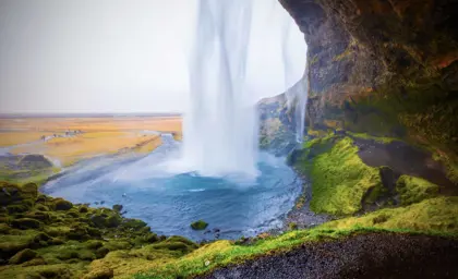 Seljalandsfoss waterfall in Iceland, cascading down a cliff with a walkway that allows visitors to walk behind the falls.
