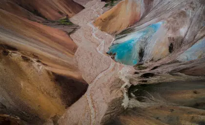 Aerial view of stream flowing through Landmannalaugar's colorful mountains, showcasing Iceland's unique volcanic landscape with red, brown, and blue hues.