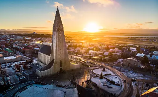 A stunning aerial view of Hallgrímskirkja at sunrise in Reykjavík, Iceland, with golden light illuminating the iconic church and cityscape. Reykjavík city tour by Travel Reykjavík.