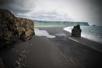 A view of Reynisfjara black sand beach with rugged cliffs and ocean waves in South Iceland.
