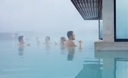 Visitors enjoying the geothermal waters of Blue Lagoon in Iceland with silica face masks, surrounded by steam and minimalistic architecture in a serene spa setting.