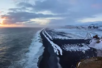 Solheimafjara Black Sand Beach Stretch in winter with snow covering the sand and a golden winter sunset in the background.