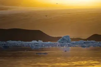 Midnight Sun in Iceland over Jokulsarlon Glacier Lagoon with floating icebergs and glacier in the background.