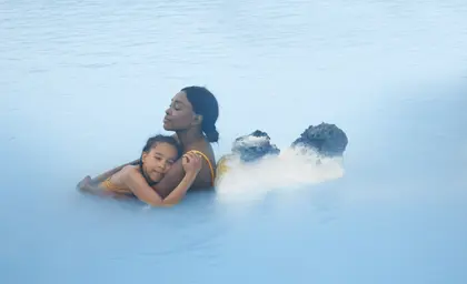 A serene moment of a mother embracing her daughter in the soothing, milky-blue waters of the Blue Lagoon in Iceland, surrounded by volcanic rocks and steam. This iconic geothermal spa is known for its mineral-rich waters and relaxing atmosphere, making it a perfect family-friendly destination.
