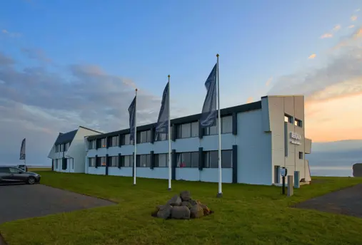 Exterior view of Berjaya Hótel in Höfn with an ocean view of the sunset in the background.