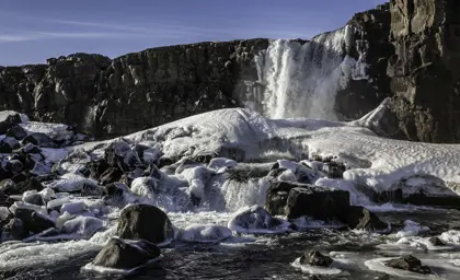 Frozen waterfall surrounded by icy rocks on a cold winter day in Iceland, ideal for glacier tours.