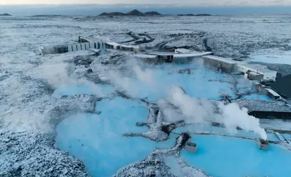 Aerial view of the Blue Lagoon geothermal spa in Iceland during winter, showcasing its steaming blue waters surrounded by a snow-covered volcanic landscape.