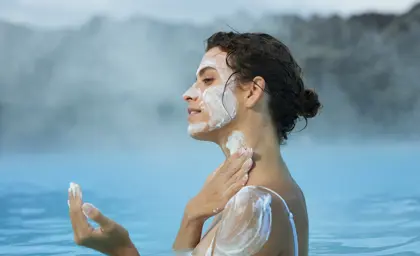 Woman applying a silica mud mask to her face while relaxing in the Blue Lagoon's soothing geothermal waters, Iceland.