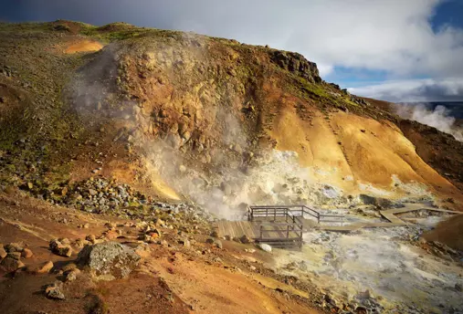 Colorful geothermal area at Krýsuvík in Iceland, with steam rising from volcanic ground and a wooden viewing platform.