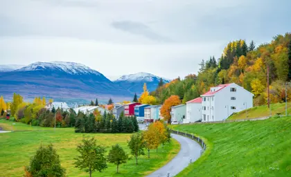 Scenic view of colorful houses in Akureyri nestled between autumn forests and snow-dusted mountains in Iceland