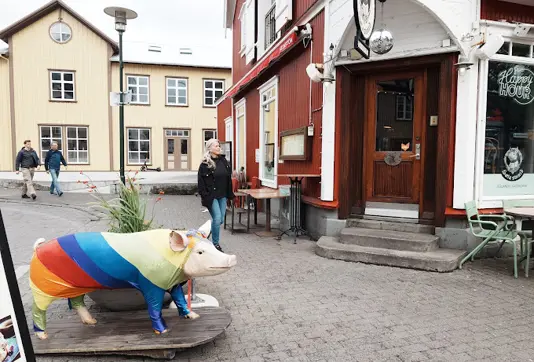 The vibrant exterior of Sæta Svínið Gastropub in downtown Reykjavík, featuring a colorful pig statue and inviting wooden entrance, perfect for a casual Icelandic dining experience.