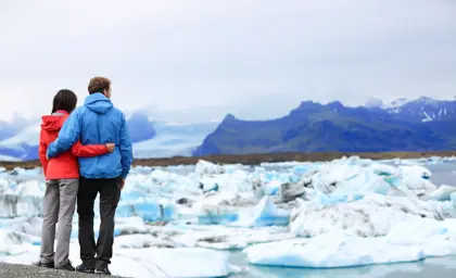 Couple dressed in red and blue jackets hugging while admiring icebergs at Jokulsarlon glacial lagoon in Iceland