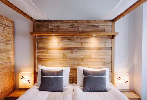  Front view of a wooden four-poster bed with bedside lamps and pillows, creating a warm ambiance at Eyja Guldsmeden Hotel.