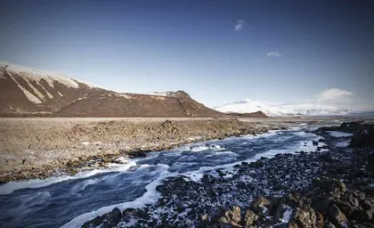 Snowy landscape view of Langjökull glacier with river stream in foreground.