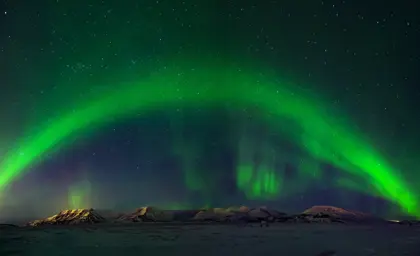 Northern lights bow over snowy mountains in Iceland.