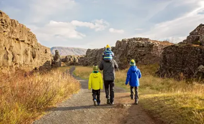 Father and three children hiking along a scenic path in Thingvellir National Park with rocky cliffs and distant mountains in autumn Iceland