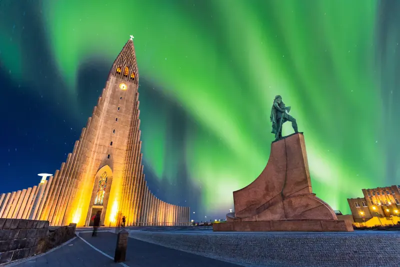 Northern lights dancing above Hallgrimskirkja Church and Leif Erikson statue in Reykjavik, Iceland, during a clear winter night.