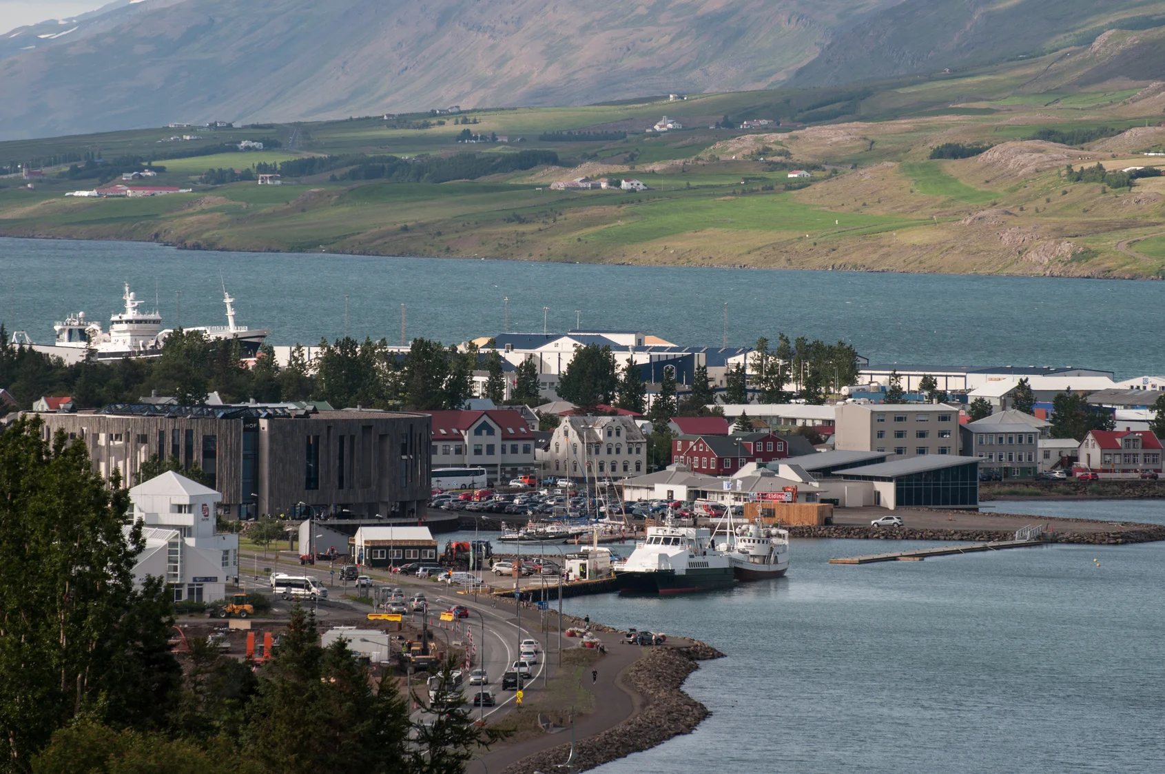 A view of Akureyri's harbor, showcasing ships docked along the coastline with the town's colorful houses and surrounding mountains in the background.