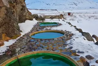 Hoffell Hot Tubs in Iceland in winter with snowcovered ground and mountain side in the background.