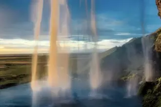 Midnight Sun in Iceland seen from behind Seljalandsfoss waterfall.