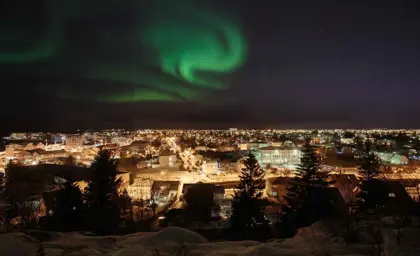 Beautiful Northern Lights swirling above the cityscape of Reykjavik at night, creating a mesmerizing view.