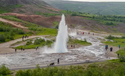 Geysir Hot Spring erupting in an Icelandic valley, surrounded by tourists capturing the natural spectacle, part of the Journey Around Iceland tour.