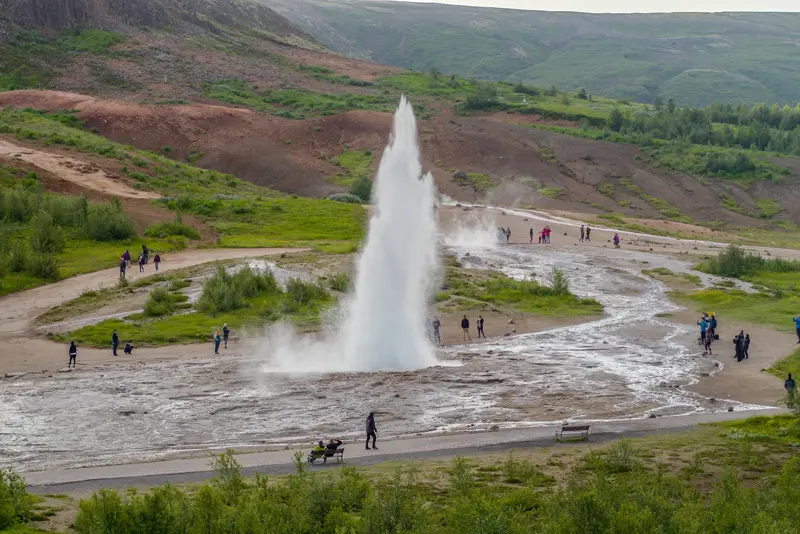 Geysir Hot Spring erupting in an Icelandic valley, surrounded by tourists capturing the natural spectacle, part of the Journey Around Iceland tour.