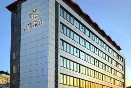 Exterior view of Reykjavík Lights Hotel, a modern multi-story building with a wave-like red roofline and large reflective windows at sunset.