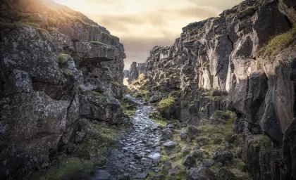 Sunlit rocky rift valley in Thingvellir National Park, showcasing moss-covered rocks and a narrow stone path, a historic site of geological and cultural significance in Iceland.