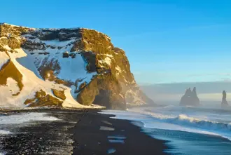 Reynisfjara black sand beach snow covered in winter with view of Sea stacks and Cave.