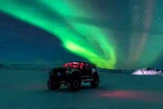 Super Jeep Under Northern Lights In Winter Snow Covered Ground Iceland.