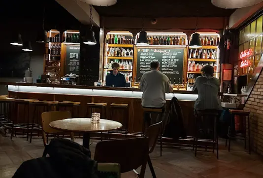 Cozy interior of Skúli Craft Bar in Reykjavik with a warm ambiance, featuring a bartender, patrons, and a display of craft beer bottles, a popular stop for locals and tourists on Iceland tours.