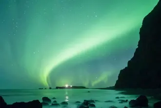Reynisfjara Black Sand Beach under green Northern Lights in Iceland.