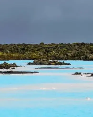The blue waters of the Blue Lagoon surrounded by moss covered rocky black lava with a rainbow rising up above.