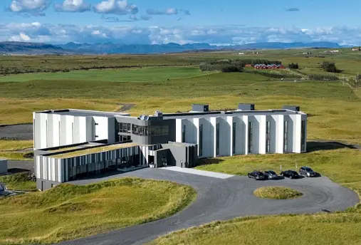 Aerial view of Landhotel, a modern, white building surrounded by Iceland’s lush green countryside with distant mountains in the background.