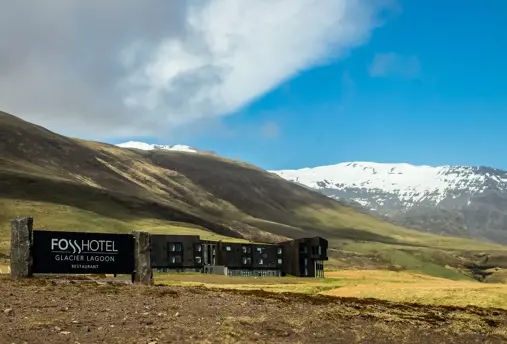 Fosshótel Glacier Lagoon exterior view with hotel sign in the foreground and mountains in the back.
