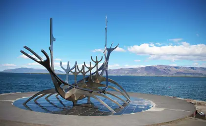 The Sólfarið Sun Voyager sculpture in Reykjavik, Iceland, set against a backdrop of blue skies and distant mountains.