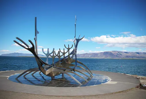The Sólfarið Sun Voyager sculpture in Reykjavik, Iceland, set against a backdrop of blue skies and distant mountains.