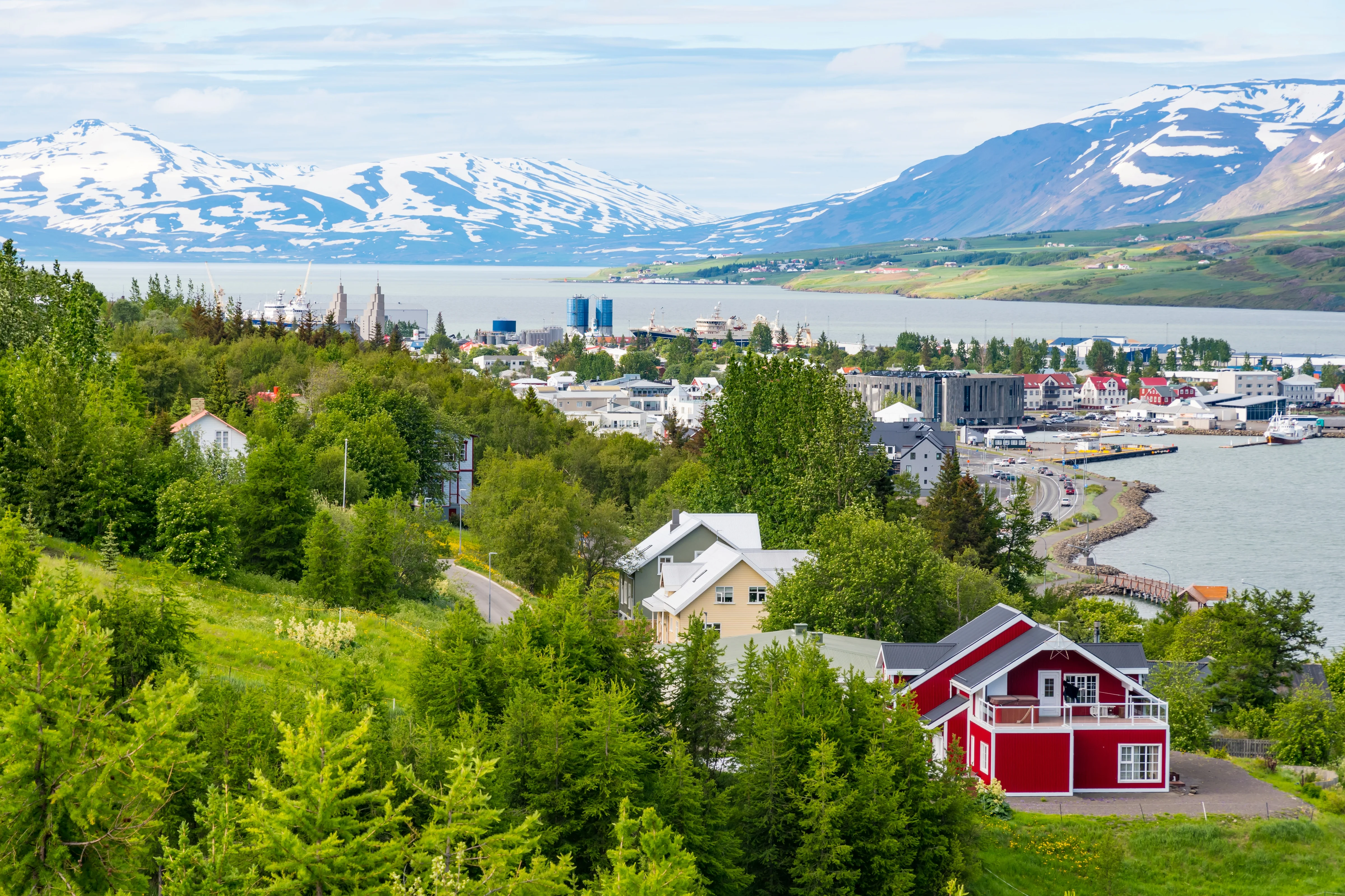Akureyri nestled in a lush green landscape with colorful houses, fjord waters, and snow-covered mountains in the distance.