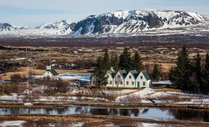 Scenic view of Þingvellir National Park with snow-covered mountains and traditional Icelandic church by the lake in early spring.