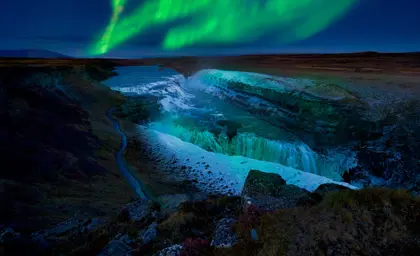 Stunning view of the Northern Lights illuminating Gullfoss waterfall in Iceland during a cold winter night.