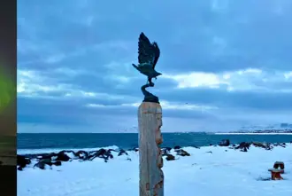Alftanes Beach with Northern Lights and snow covered ground in winter.
