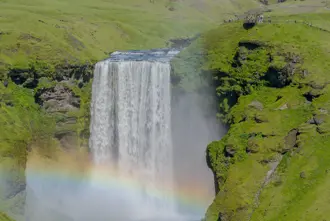 Skógafoss waterfall in south Iceland with rainbow and green mossy ground around.