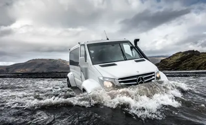 A close-up view of a Travel Reykjavík superjeep fording a river, with water rushing around its wheels, highlighting the excitement and rugged terrain of the Icelandic highlands.